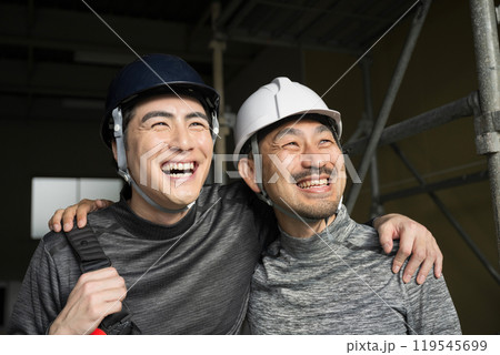 現場作業員(鳶職や屋外の安全帯ハーネスをつけた）の肩を組むガテン系仲良し2人の見上げる笑顔　 119545699