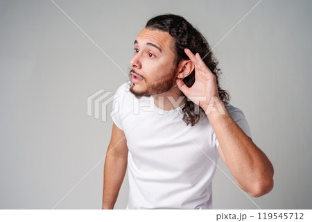 A young man with curly hair listening attentively while standing against a plain background A young man with curly hair listening attentively while standing against a plain background 119545712