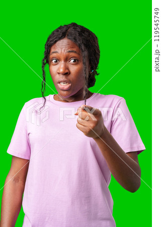 A surprised woman poses dramatically with hands on her chest in front of a bright green background 119545749