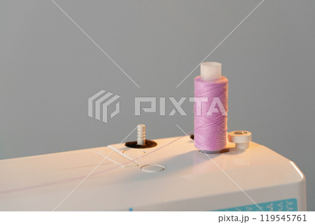 View of a sewing machine with a spool of pink thread placed on top 119545761