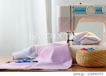 Sewing machine in use on a wooden table, stitching a light fabric in a well-lit indoor workspace 119545772
