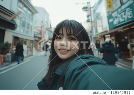 Young woman smiling and taking a selfie on a bustling street in a vibrant urban area during the 119545931