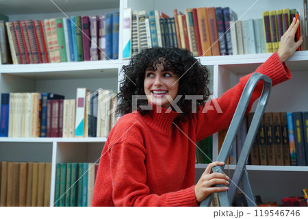 Brunette curly-haired young woman on the ladder at the bookshelves 119546746