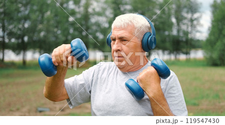 Old man exercising with dumbbells outside. Physical therapy. Elderly 60s male working out. Active sporty gray haired man standing with weights. Older person doing fitness outdoors. People, gym, sport 119547430