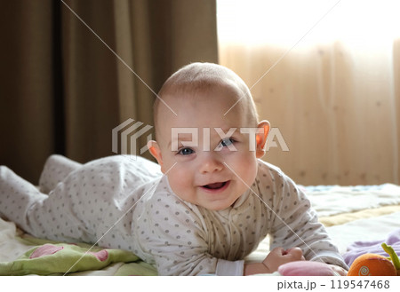 Smiling baby girl learning to crawl and playing with colorful toys in white sunny bedroom. 119547468