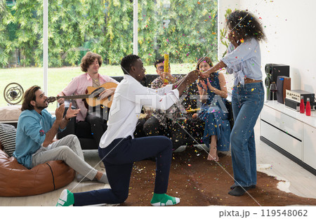 Friends celebrating party with colorful confetti in living room at home. Diversity group drinking and playing music Friends celebrating party with colorful confetti in living room at home. Diversity group drinking and playing music 119548062