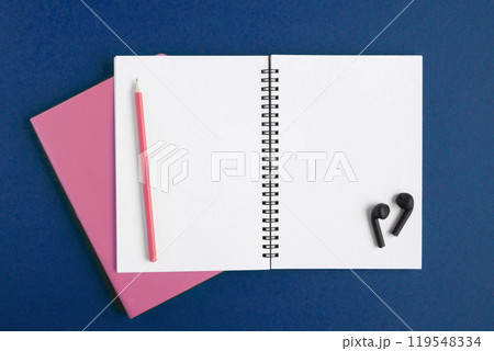 Notebook and pencil, wireless headphones. Open notebook on dark blue color background, spiral notepad. Top view. Notepad with blank white pages for write, office flat lay. Copy Space. Navy. To do list 119548334