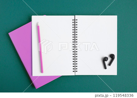 Notebook with pencil, wireless headphones. Open notebook on dark green color background, spiral notepad. Top view. Notepad with blank white pages for write, office flat lay. Copy Space. To do list 119548336