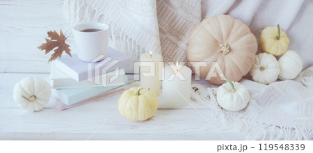 Autumn still life with pumpkins, a cup of coffee, books, candles and autumn leaves on a white wooden background 119548339