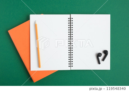 Notebook with pencil, wireless headphones. Open notebook on dark green color background, spiral notepad. Top view. Notepad with blank white pages for write, office flat lay. Copy Space. To do list 119548340