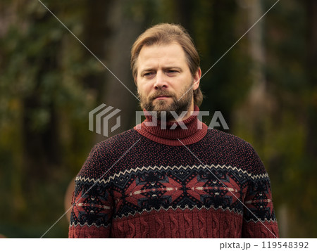 Portrait of handsome young man in wool knitted sweater outdoors. Male with long hair and beard feel happy, calm and serious on Green nature background. Man looking away into distance. Diversity People 119548392