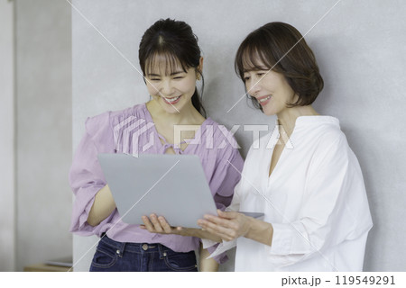 ノートパソコンを手に会話する若い女性とミドルエイジの女性 119549291