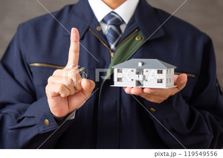 マンションの模型を持って人差し指を立てる作業着を着たミドル男性ビジネスマン マンションの模型を持って人差し指を立てる作業着を着たミドル男性ビジネスマン 119549556