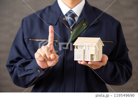 住宅模型を持って人差し指を立てる作業着を着たミドル男性ビジネスマン 119549690