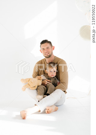 Young father and little son are sitting on the floor. Scene is warm and affectionate, as the man and child are sharing a close moment together 119550022
