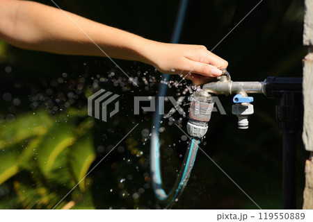 Woman hand opening hose faucet with water leak in a garden Woman hand opening hose faucet with water leak in a garden 119550889