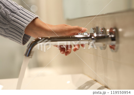 Woman hand opening faucet in a bathroom Woman hand opening faucet in a bathroom 119550954