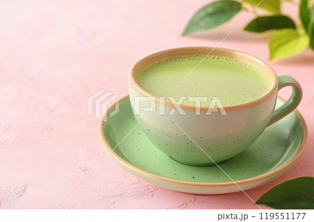A vibrant green cup of matcha tea placed on a pastel pink surface with a touch of greenery A vibrant green cup of matcha tea placed on a pastel pink surface with a touch of greenery 119551177