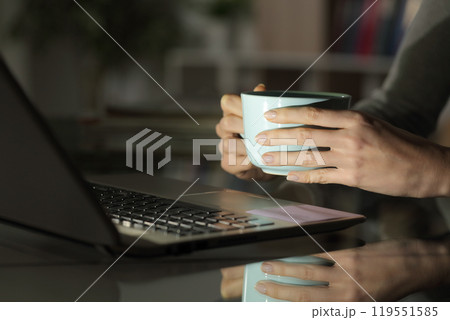 Girl hands watching media on laptop at night with coffee Girl hands watching media on laptop at night with coffee 119551585