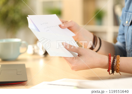 Student girl hand putting letter on an envelope at home Student girl hand putting letter on an envelope at home 119551640