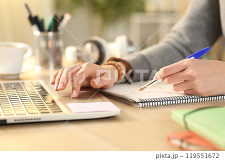 Student hands comparing notes on notebook with laptop Student hands comparing notes on notebook with laptop 119551672