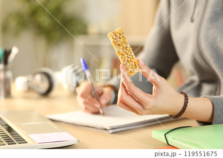 Student hands holding cereal snack bar studying 119551675