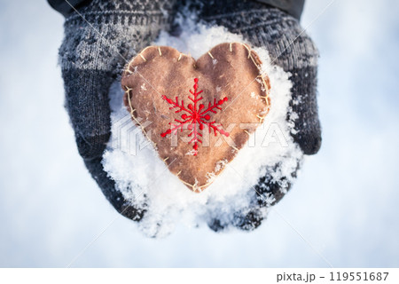 Hands in gloves holding a handmade heart ornament with a snowflake embroidery Hands in gloves holding a handmade heart ornament with a snowflake embroidery 119551687
