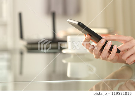 Woman hand using wifi on phone with a router in background Woman hand using wifi on phone with a router in background 119551819
