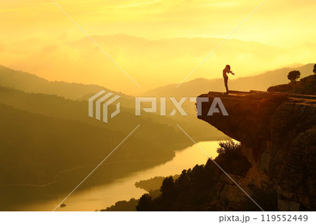 Woman silhouette breathing fresh air in the top of a cliff 119552449