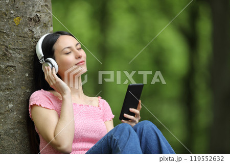Asian woman listening to music in a forest Asian woman listening to music in a forest 119552632
