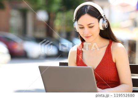 Asian woman wearing headphone using laptop in the street 119552680