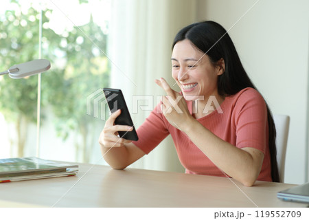 Happy asian woman crossing fingers checking phone in a desk Happy asian woman crossing fingers checking phone in a desk 119552709