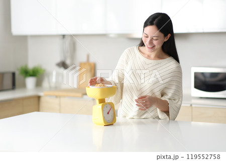Happy asian woman weighing cereals standing in the kitchen 119552758
