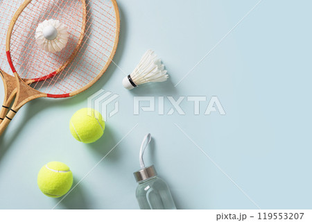 Concept racket sport. Badminton rackets, tennis balls ,water bottle and white feather badminton shuttlecocks on blue background. View from above. Leisure games. Copy space. 119553207