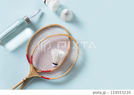 Wooden badminton rackets, water bottle and white feather badminton shuttlecocks on blue background. View from above. Concept racket sport. Leisure games. Copy space. Wooden badminton rackets, water bottle and white feather badminton shuttlecocks on blue background. View from above. Concept racket sport. Leisure games. Copy space. 119553210