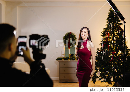 A beautiful woman in a shiny dress with a microphone at the Christmas tree singing song and recording video. The singer's performance at the New Year's holiday 119555354