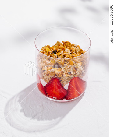 Glass filled with yogurt, granola and strawberries is standing on white surface 119555690