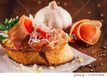 Delicious bruschetta with parma ham, cheese, tomatoes and arugula on wooden table Delicious bruschetta with parma ham, cheese, tomatoes and arugula on wooden table 119555969