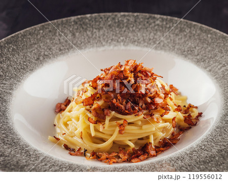Delicious pasta dish with fried bacon on top served on elegant restaurant plate 119556012