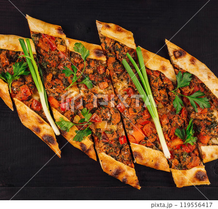 Turkish pide with minced meat and vegetables lying on black wooden table Turkish pide with minced meat and vegetables lying on black wooden table 119556417