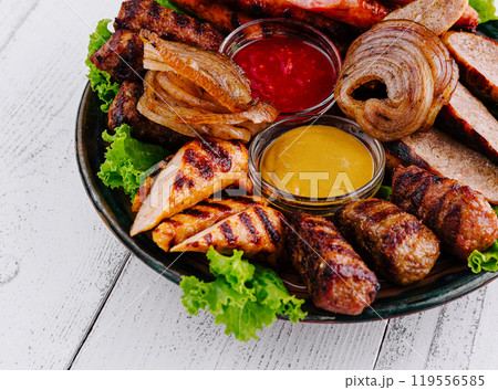 Grilled meat platter with sausages, chicken, and kebabs with dipping sauces 119556585