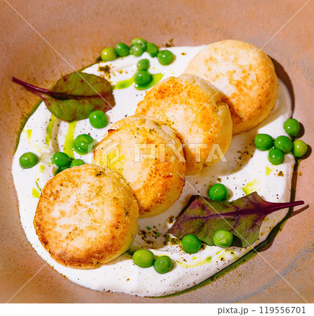 Cottage cheese pancakes lying on white sauce and decorated with green peas and beet leaves 119556701