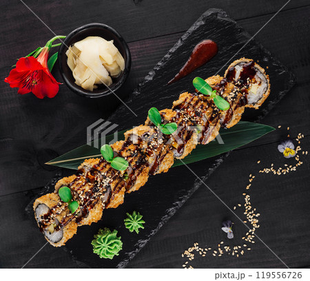 Tempura maki sushi rolls covered with sesame seeds and unagi sauce lying on black stone plate 119556726