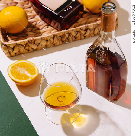 Bottle and glass of cognac with lemons on white and green background Bottle and glass of cognac with lemons on white and green background 119557012