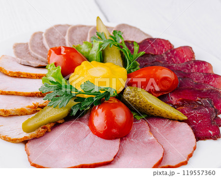 Plate combining several types of meat cuts and pickles being served on white table Plate combining several types of meat cuts and pickles being served on white table 119557360