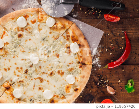 Delicious four cheese pizza lying on wooden table surrounded by fresh ingredients Delicious four cheese pizza lying on wooden table surrounded by fresh ingredients 119557420