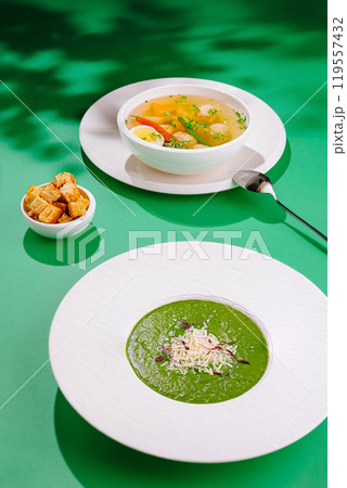 Two bowls of hot soup served on a green tablecloth with croutons on the side 119557432