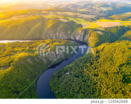 A vibrant sunset casts golden hues over the tranquil Vltava River, meandering through lush green hills of Czechia, creating a breathtaking natural landscape during evening hours. A vibrant sunset casts golden hues over the tranquil Vltava River, meandering through lush green hills of Czechia, creating a breathtaking natural landscape during evening hours. 119562689