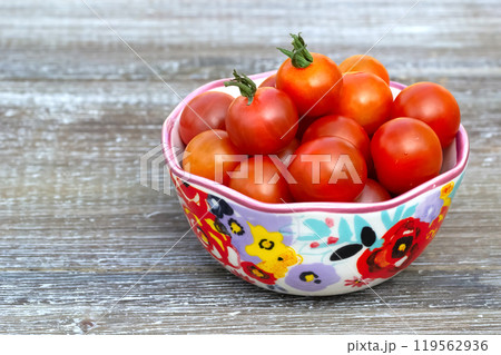 Red cherry tomatoes in a bowl with floral pattern. 119562936