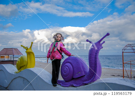 Girl and snails against the backdrop of a seascape. On the Odessa embankment there are decorative snails and a girl against the backdrop of a cloudy sky. 119563179